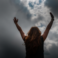 daytime, dark clouds with sunbeam shining through the clouds, woman with arms outstretched to sky in victory and joy
