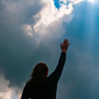 daytime, dark clouds with sun shining through the clouds like a beacon, woman with arms outstretched to sky in victory and joy