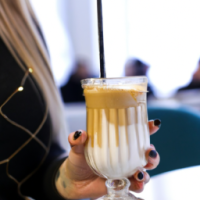 a close up of a vanilla latte in a tall glass wih  a straw in a ladies hands