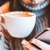 a close up of a woman siipping from a mug of  vanilla latte while scrolling on her phone