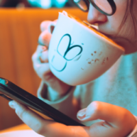 a close up of a woman siipping from a mug of  vanilla latte while scrolling on her phone