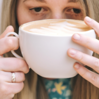 a close up of a woman siipping from a mug of  vanilla latte holding it with both hands