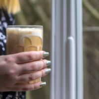 a close up of a woman holding a clear glass of  vanilla latte looking out her kitchen window