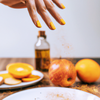 vertical smartphone-style photo of a wooden kitchen counter with simple home remedy ingredients arranged neatly, round white plate in foreground filled with fresh orange slices, a woman’s hand with neat polished nails sprinkling reddish powder over the slices mid-motion, powder particles visible in the air, behind the plate a bottle of apple cider vinegar, a small turmeric spice jar, and a baking soda box, casual kitchen setting, natural indoor lighting, soft shadows, realistic textures, health hack aesthetic, social media wellness post look, slight depth of field blur in background, photorealistic, warm tones --ar 9:16 --v 6 --style raw --quality 2