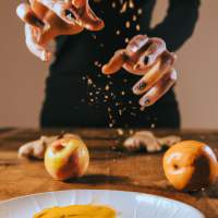 vertical smartphone-style photo of a wooden kitchen counter with simple home remedy ingredients arranged neatly, round white plate in foreground filled with fresh orange slices, a woman’s hand with neat polished nails sprinkling reddish powder over the slices mid-motion, powder particles visible in the air, behind the plate a bottle of apple cider vinegar, a small turmeric spice jar, and a baking soda box, casual kitchen setting, natural indoor lighting, soft shadows, realistic textures, health hack aesthetic, social media wellness post look, slight depth of field blur in background, photorealistic, warm tones --ar 9:16 --v 6 --style raw --quality 2