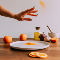 vertical smartphone-style photo of a wooden kitchen counter with simple home remedy ingredients arranged neatly, round white plate in foreground filled with fresh orange slices, a woman’s hand with neat polished nails sprinkling reddish powder over the slices mid-motion, powder particles visible in the air, behind the plate a bottle of apple cider vinegar, a small turmeric spice jar, and a baking soda box, casual kitchen setting, natural indoor lighting, soft shadows, realistic textures, health hack aesthetic, social media wellness post look, slight depth of field blur in background, photorealistic, warm tones --ar 9:16 --v 6 --style raw --quality 2