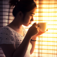 a women drinking coffee -looking curios Standing in a window with a soft golden light . curtain open to reveal the morning light . want the theme to be the most powerful part of day 