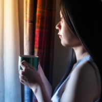 a women drinking coffee -looking curios Standing in a window with a soft golden light . curtain open to reveal the morning light . want the theme to be the most powerful part of day 