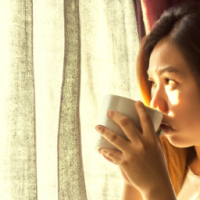 a women drinking coffee -looking curios Standing in a window with a soft golden light . curtain open to reveal the morning light . want the theme to be the most powerful part of day 