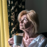 a english women in 50's drinking coffee -looking curios Standing in a window with a soft golden light . curtain open to reveal the morning light . want the theme to be the most powerful part of day 