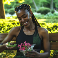 A MODEL TYPE BEAUTIFUL DARK SKINNED BLACK WOMAN WITH BRAIDS IN HER HAIR WITH A HEALTHY APPEARANCE EATING A SALAD AND DRINKING WATER ON A PARK BENCH SMILING WHILE LOOKING AT BEAUITFUL FLOWERS YOU