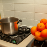 A pot overflowing with boiling oranges in a kitchen with vegetables on the bench