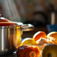 A pot overflowing with boiling orange peels in a kitchen with vegetables on the bench