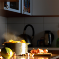 A pot overflowing with boiling orange peels in a kitchen with vegetables on the bench