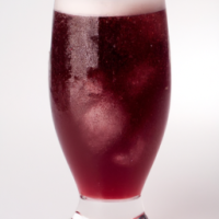 tall glass or dark red juice with ice and foam on top