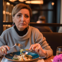 A middle aged woman, sitting in a casual restaurant, eating a salad.