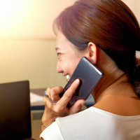 An over the shoulder view of an attractive 26 year old Thai woman typing on her laptop with a mobile phone on the side