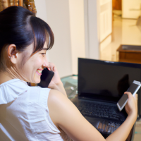 An over the shoulder view of an attractive 26 year old Thai woman typing on her laptop with a mobile phone on the side